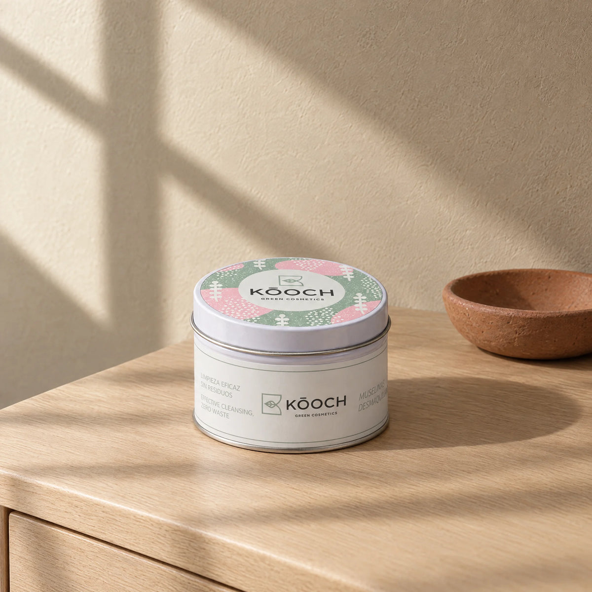 Lata de muselinas Kōoch edición Invierno, con tapa rosa y verde salvia, sobre una cómoda de roble junto a un platito de barro